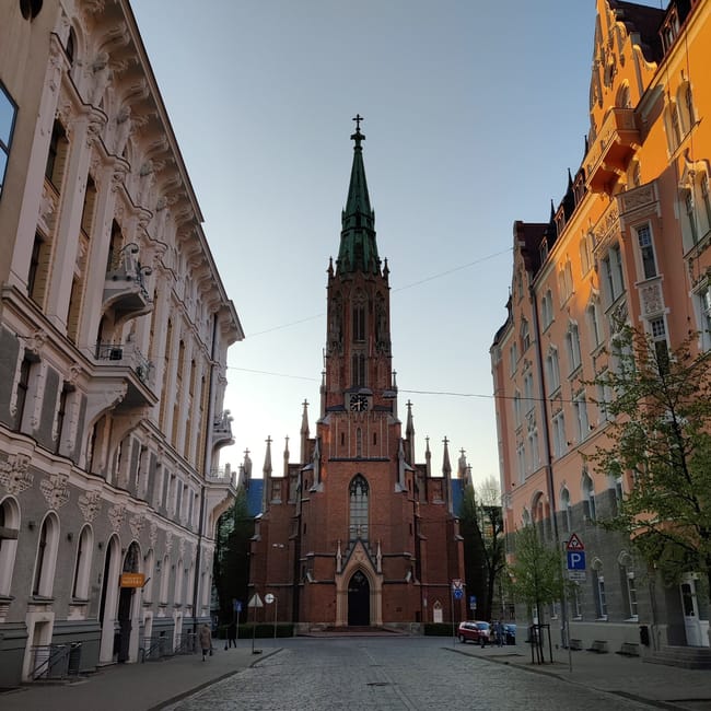 Kościół św. Jana w rydze widziany między kamienicami przy brukowanej ulicy.