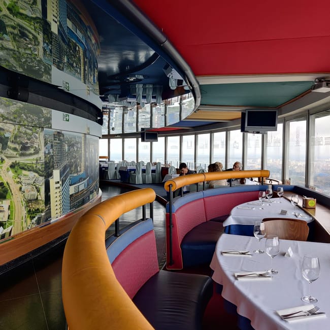 Panoramiczna restauracja z widokiem na wilno, z kolorowymi ławkami i nakrytymi stolikami.