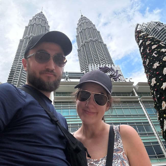 Para turystów na tle wież petronas towers w kuala lumpur, obok świątecznej choinki.