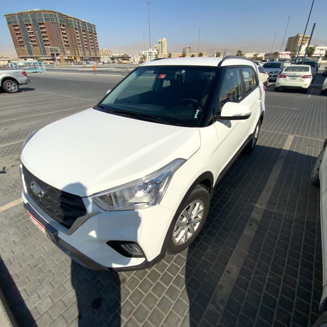Biały suv na parkingu w ras al khaimah, z zabudową miasta w tle