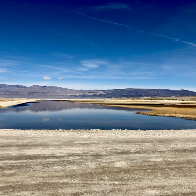 Death valley: słona równina z płytkim, spokojnym zbiornikiem wodnym i górami w tle.