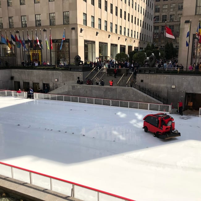 Lodowisko rockefeller center w nowym jorku, z maszyną do wygładzania lodu i flagami wokół.