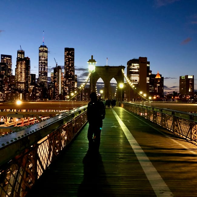 Most brooklyński o zmierzchu z sylwetką przechodnia i panoramą manhattanu w tle