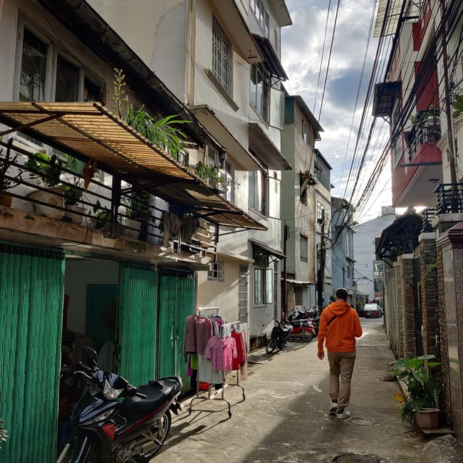 Wąska uliczka w da lat z blokami mieszkalnymi, skuterami i przechodniem w pomarańczowej bluzie