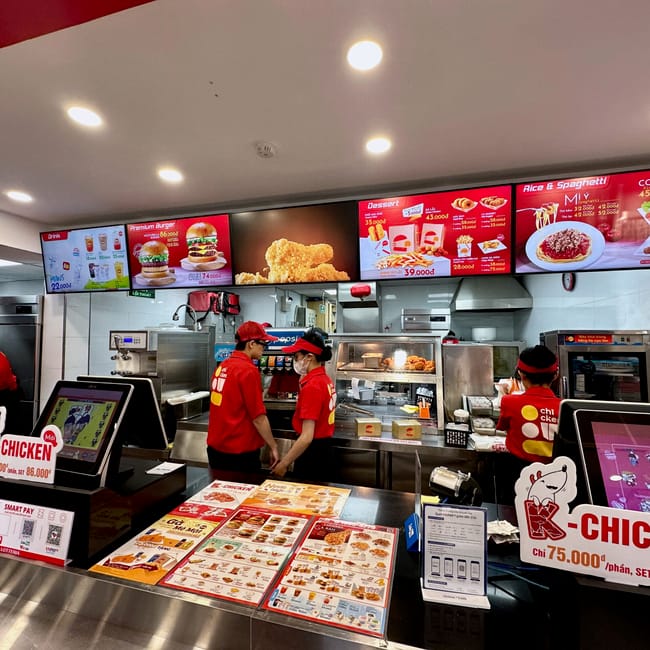Wnętrze restauracji lotteria w da lat z pracownikami przy ladzie i podświetlonym menu.