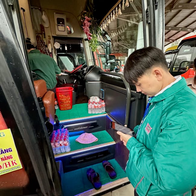 Wnętrze autobusu na dworcu autobusowym w da lat, obok młody mężczyzna w zielonej kurtce patrzy w telefon.
