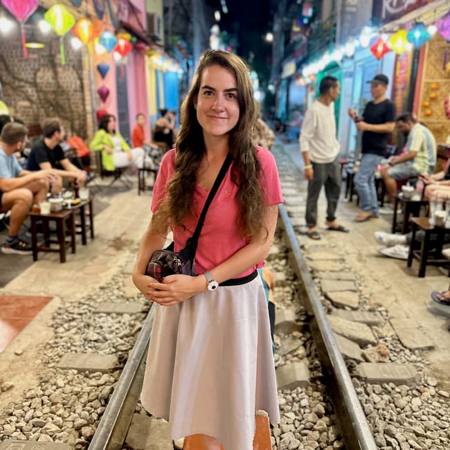 Kobieta stoi na torach na hanoi train street w hanoi, otoczona kolorowymi lampionami i kawiarniami.