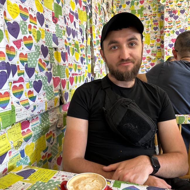 Mężczyzna siedzi w the note cafe w hanoi, otoczony ścianami pokrytymi kolorowymi karteczkami i sercami.