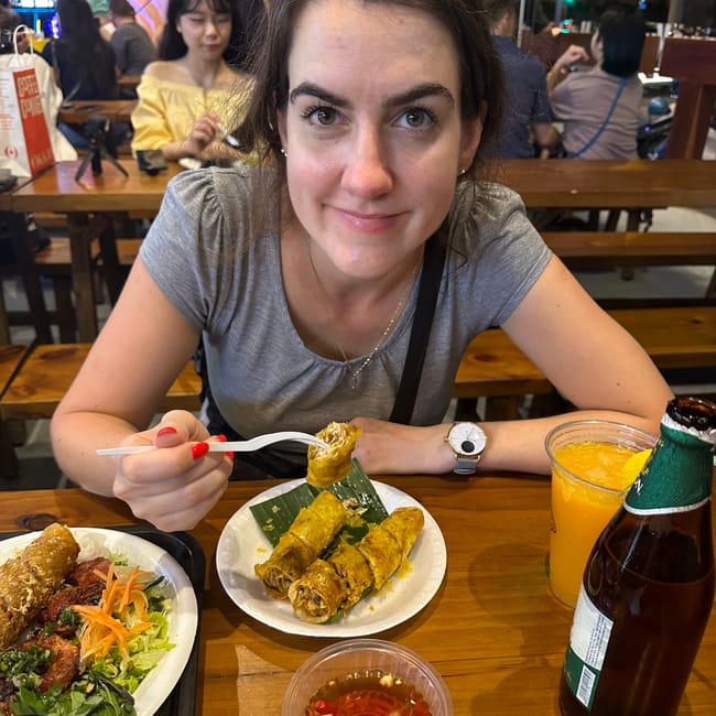 Kobieta je w restauracji w ho chi minh foods, przed nią wietnamskie dania, sos i napój pomarańczowy.