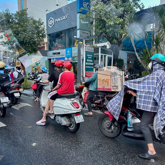 Ruchliwa ulica w ho chi minh z kierowcami skuterów przed salonem piaggio i vespa.