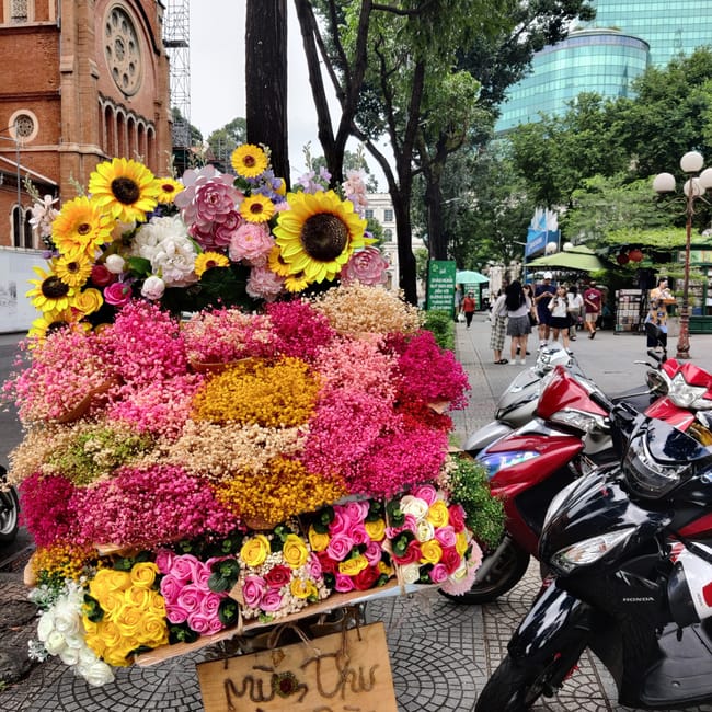 Kwiatowy stragan na skuterze w ho chi minh, obok czerwonego kościoła i nowoczesnych wieżowców