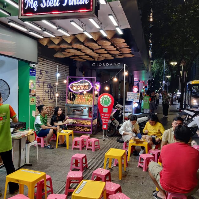 Uliczne jedzenie przy ho chi minh square w wietnamie, z neonowym szyldem i plastikowymi stolikami.