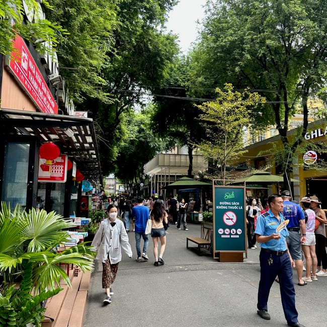 Book street w ho chi minh pełna spacerujących ludzi, księgarni i zielonych drzew.