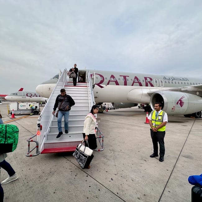 Pasażerowie schodzą po trapie z samolotu qatar airways na płycie lotniska w dosze.