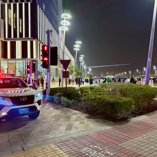Nocna ulica w doha z radiowozem, sygnalizacją i tłumem pieszych przy nowoczesnych budynkach