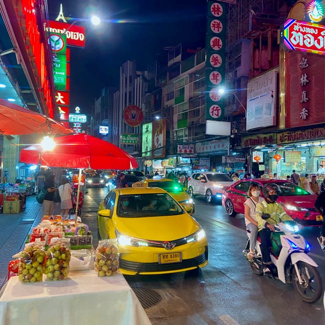 Nocny ruch na ulicy w bangkoku z taksówką, skuterem i stoiskami z owocami w chinatown.