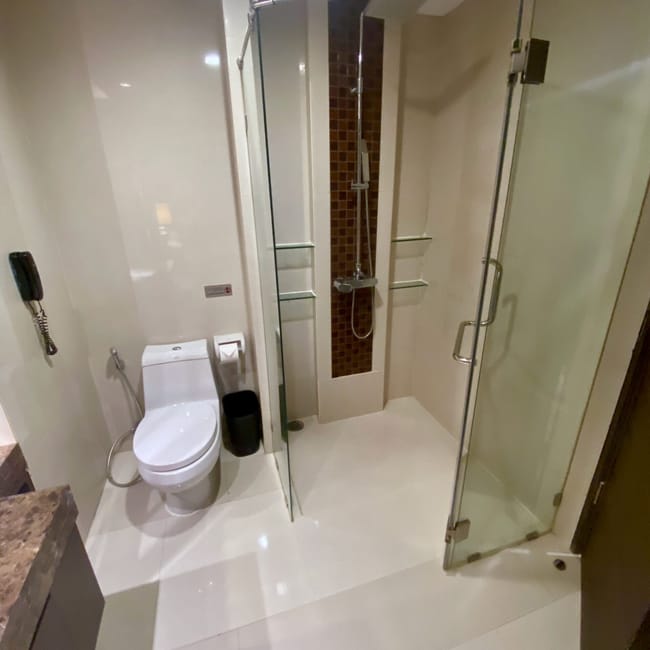 Łazienka hotelowa w bangkoku z prysznicem za szklaną ścianką i toaletą.