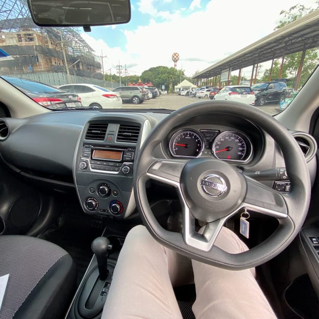 Inside a nissan car in chiang mai, thailand, with the steering wheel and dashboard visible in a parking lot