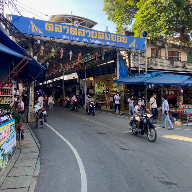 Wejście do sai lom joy walking street na targu w chiang rai, z ruchliwą ulicą i skuterami.