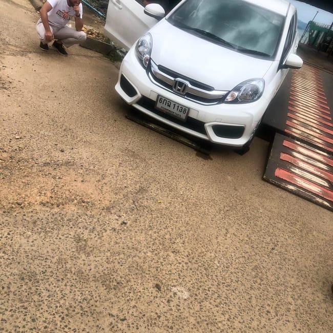 Biały samochód honda na rampie promowej w koh chang w tajlandii, obok kuca mężczyzna.