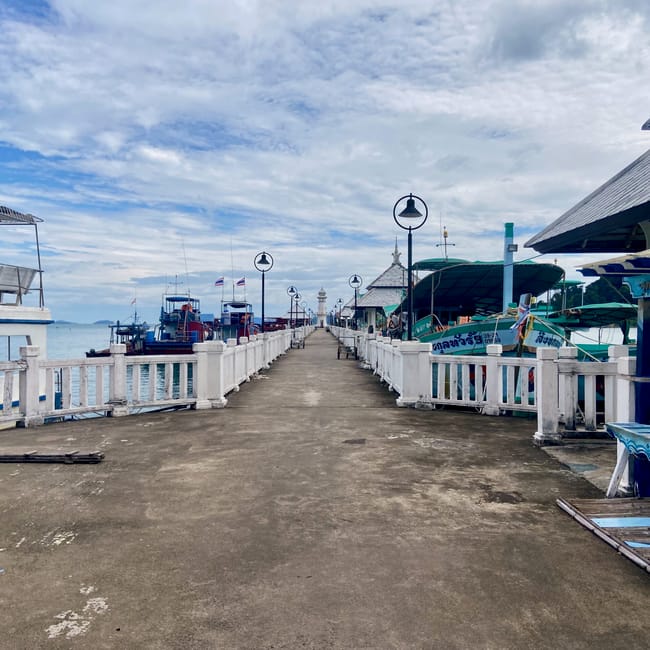 Molo na koh chang z łodziami i lampami pod pochmurnym niebem.