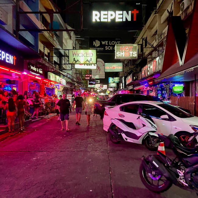 Neon-lit street in pattaya with a white sports car parked near bars and the repent sign overhead