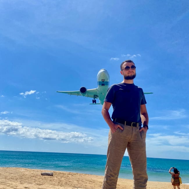 Phuket airport view: samolot nisko przelatuje nad plażą, a mężczyzna stoi na piasku pod błękitnym niebem.