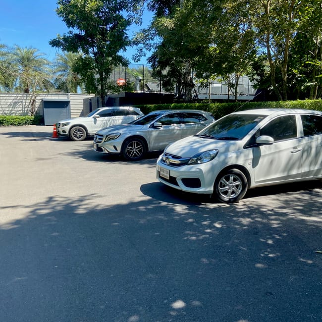 Parking z trzema białymi samochodami w ratchasima, otoczony drzewami w słoneczny dzień