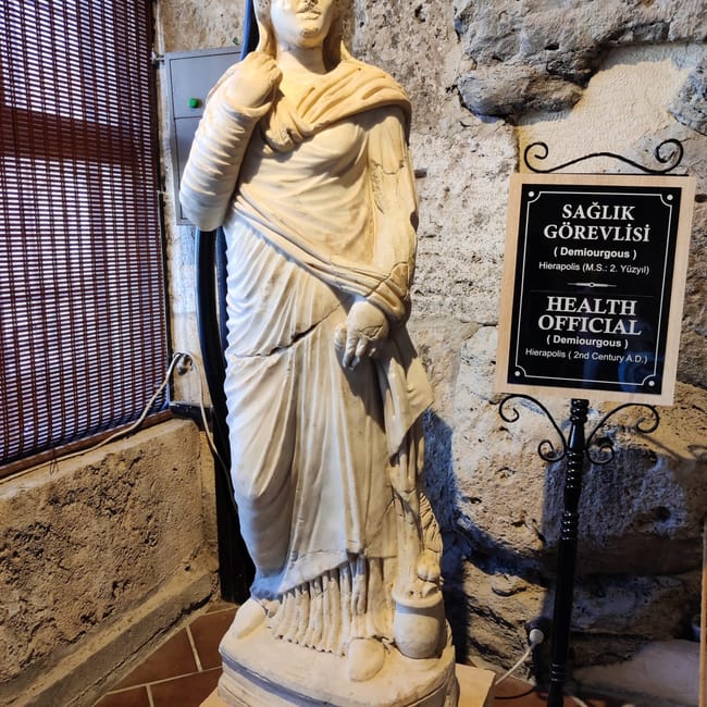 Rzeźba „health official” w muzeum archeologicznym hierapolis w pamukkale, obok tablicy informacyjnej.