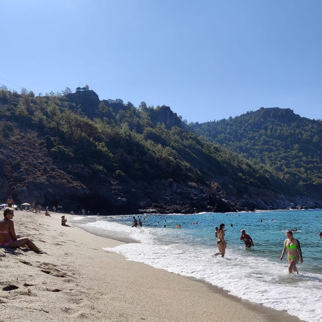 Plaża kleopatry na tureckiej riwierze, z kąpiącymi się turystami i skalistymi wzgórzami w tle