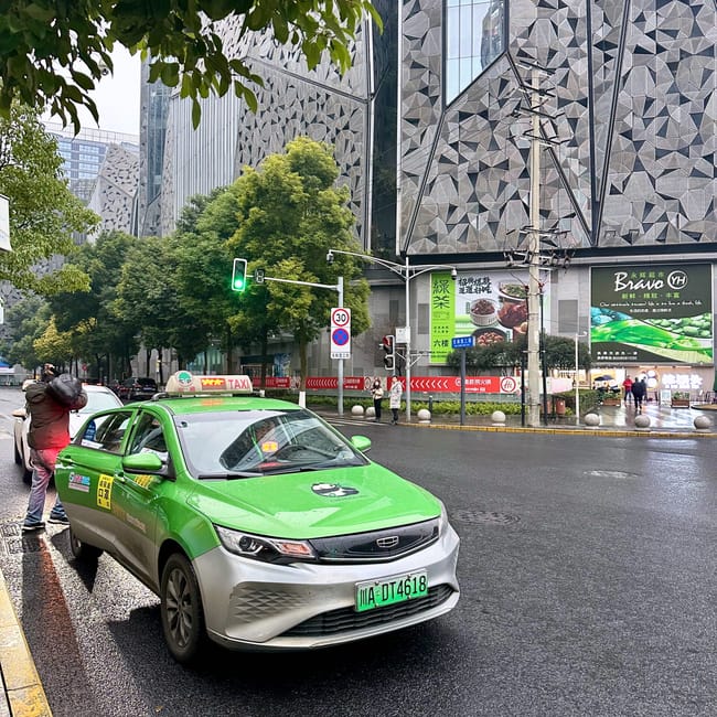 Zielona taksówka na mokrej ulicy w chengdu, na tle nowoczesnych budynków.
