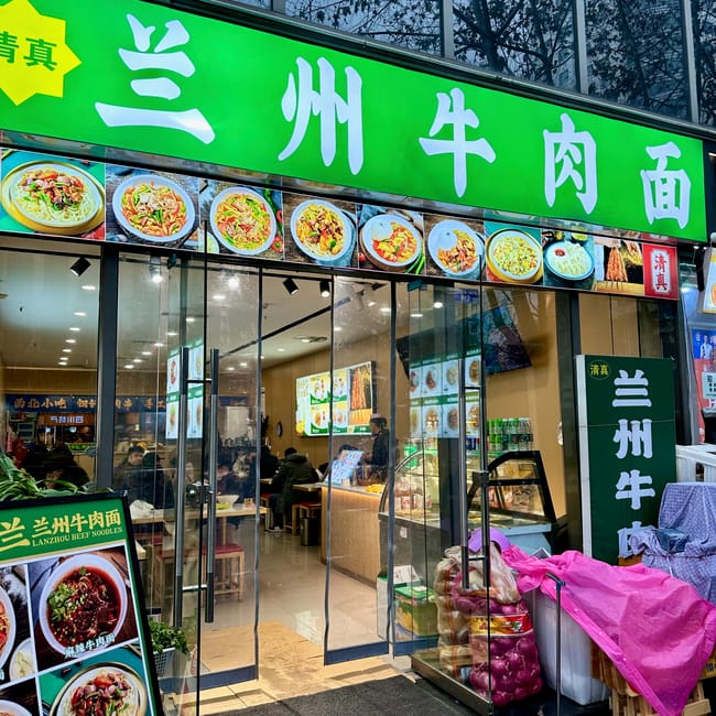 Wejście do restauracji z zielonym szyldem „兰州牛肉面” w chengdu, z menu i zdjęciami dań na witrynie