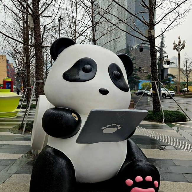 Duży posąg pandy czytającej tablet w chengdu, w deszczowej ulicznej scenerii.