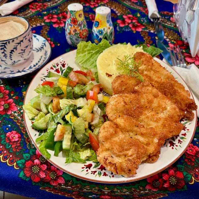 Polka restaurant w doha: talerz z kotletem, puree i sałatką oraz filiżanka kawy na kwiecistym obrusie