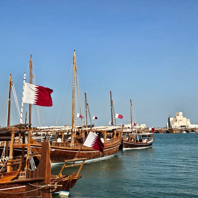 Doha corniche w katarze z drewnianymi łodziami dhow i flagami kataru na spokojnej wodzie