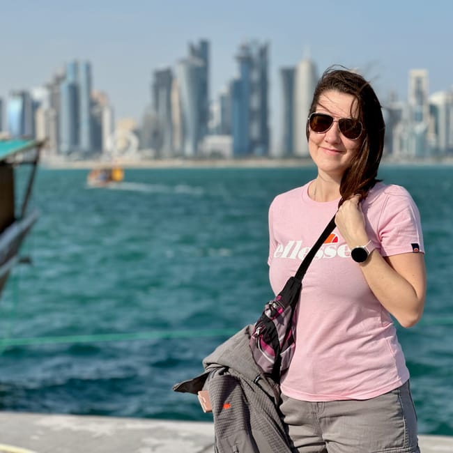 Kobieta w okularach przeciwsłonecznych stoi na doha corniche z panoramą wieżowców w tle.