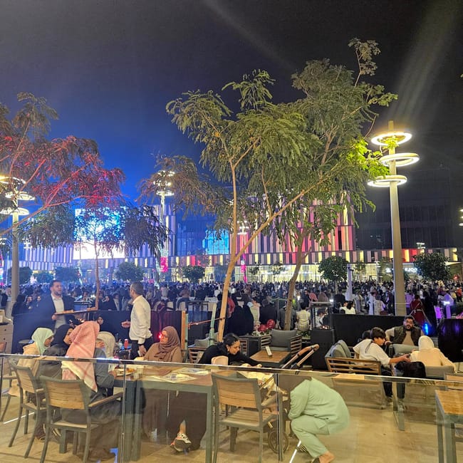 Lusail boulevard w dosze nocą, tłumy przy kawiarniach i kolorowo podświetlone budynki.