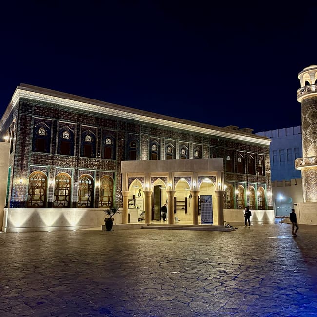 Katara cultural village w dosze nocą, podświetlony budynek z wieżą i dziedzińcem.