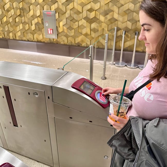 Kobieta przykłada kartę do bramki w metrze doha, trzymając napój i kurtkę.