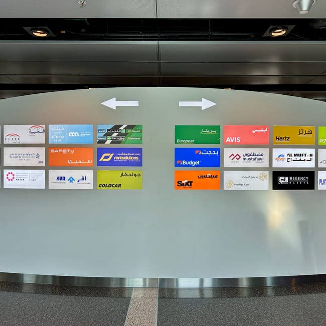 Tablica wypożyczalni samochodów w doha z logo wielu firm i strzałkami kierunku.