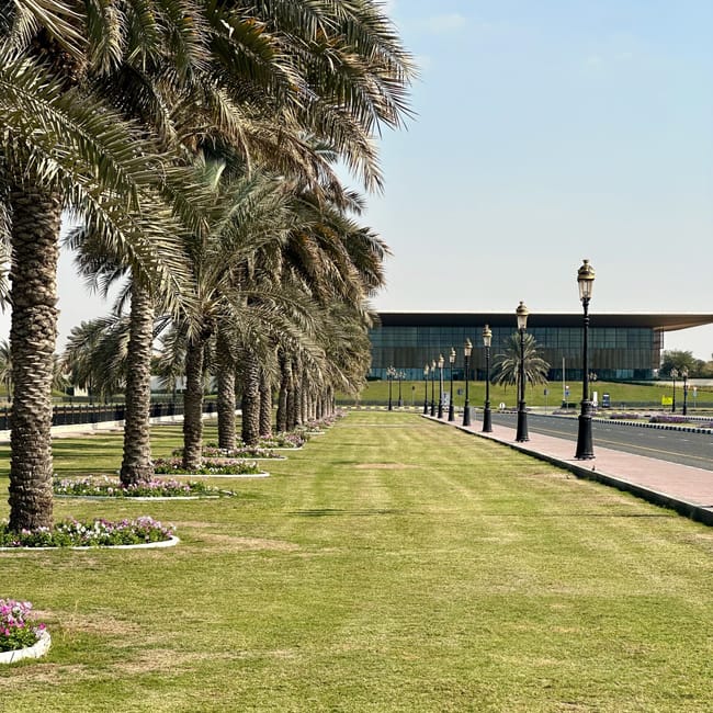 Monument sharjah arab cultural capital z palmową aleją i nowoczesnym budynkiem w tle.