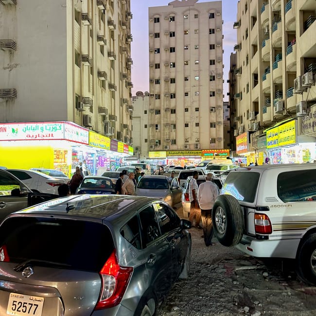 Tłoczny al ghuwair market w sharjah, z zaparkowanymi autami i sklepami między wysokimi budynkami.
