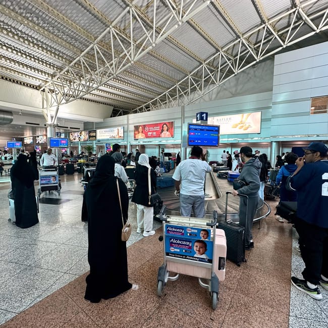 Hala przylotów na lotnisku w sharjah, z pasażerami i wózkami bagażowymi.