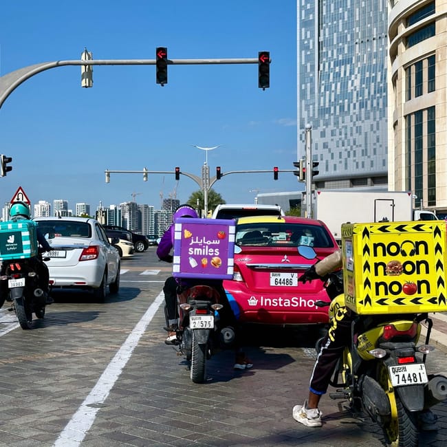 Kurierzy na skuterach czekają na światłach przy ulicy w sharjah, z wysokimi budynkami w tle