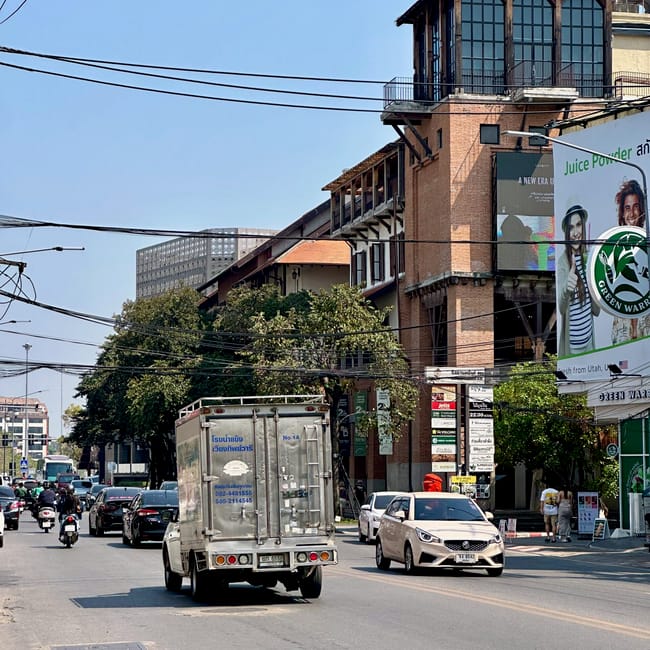 Ulica w chiang mai z ruchem ulicznym i ceglanym budynkiem z wieżą w tle