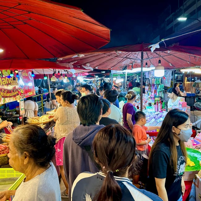 Targ nocny chiang mai night market w tłumie kupujących pod czerwonymi parasolami.