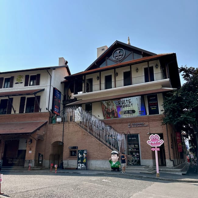 One nimman w chiang mai z ceglanym budynkiem, zewnętrznymi schodami i szyldami sklepów.