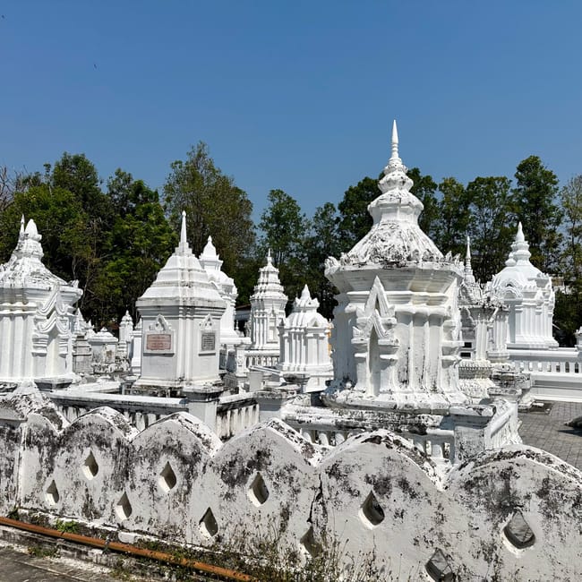 Białe stupy w wat suan dok w chiang mai, otoczone drzewami pod błękitnym niebem.