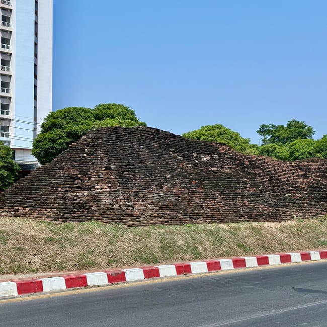 Brama suan dok gate w chiang mai, otoczona ulicą, drzewami i nowoczesnym budynkiem.