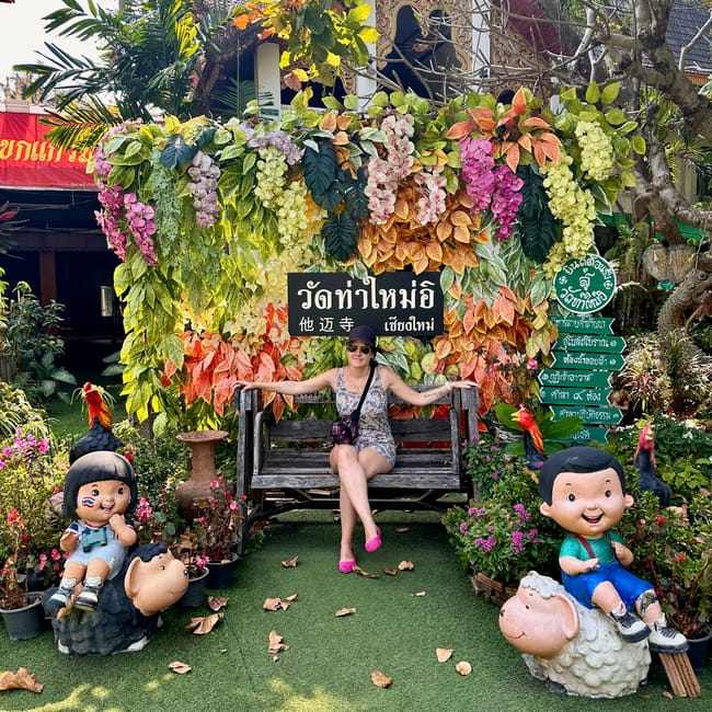 Wat tha mai w chiang mai, ozdobna ławeczka z kwiatami i figurkami dzieci na tle świątyni